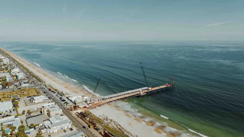 Aerial view of a fishing pier being rebuilt, reaching out over the ocean