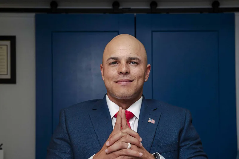 Josh Johnson of Josh Johnson Law at his desk in a navy suit, hands together, in front of blue barn doors