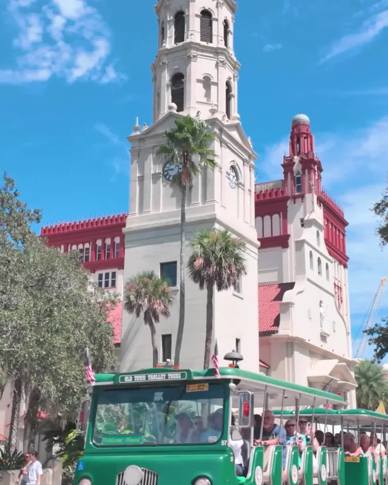 A green and red trolley in front of a historic church tower