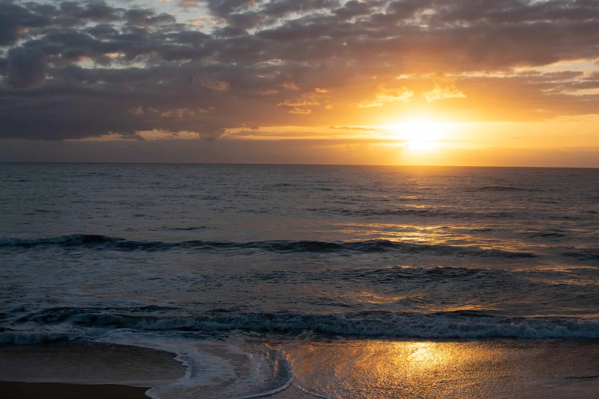 The sun breaking under a lid of cloud at sunrise, with a sheet of wave on the sand mirroring it