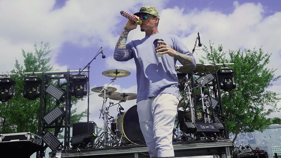 The artist on stage with the microphone raised, shot from a low angle against a big sky with the drum kit behind him