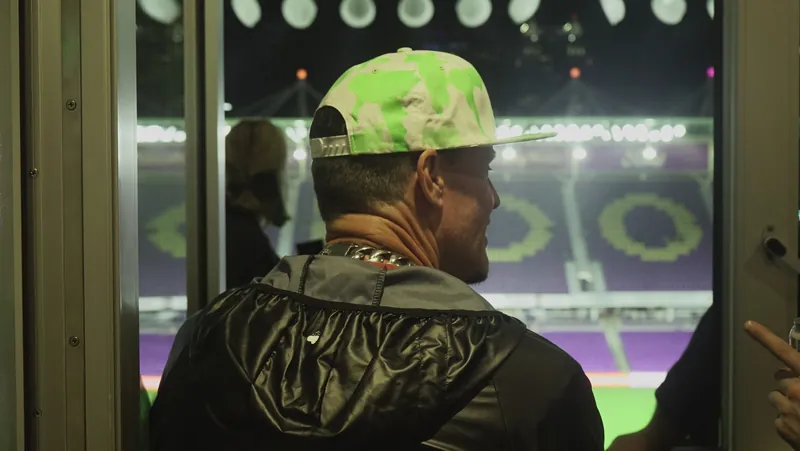 Looking over a shoulder through a window at the lit stadium pitch at night