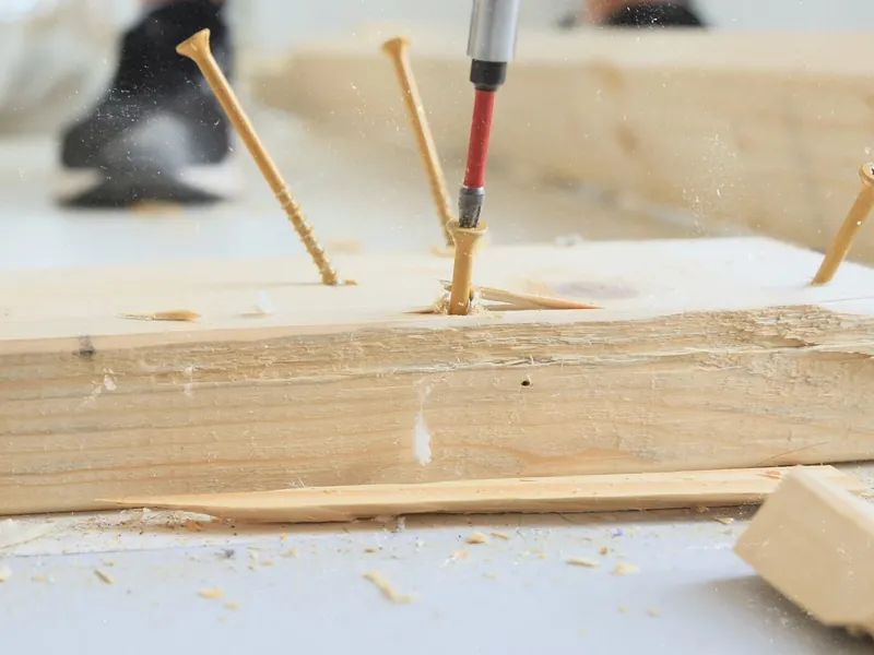 A driver setting wood screws into a length of lumber on a dusty floor