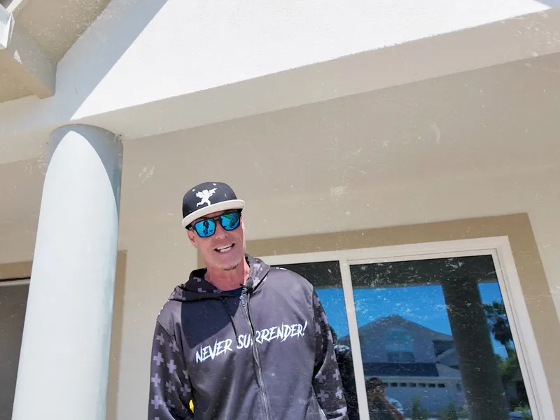 Vanilla Ice on the front porch of a house under construction, beside a white column