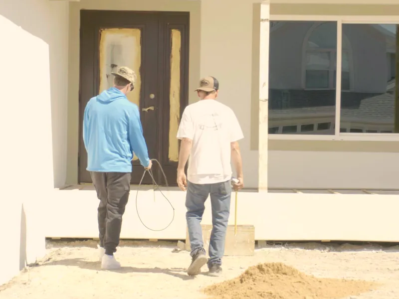 Two workers seen from behind walking up to the front door of a house under construction