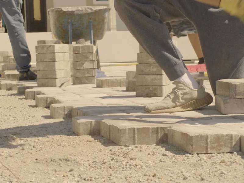 A worker kneeling to lay pavers in rows on a sandy base