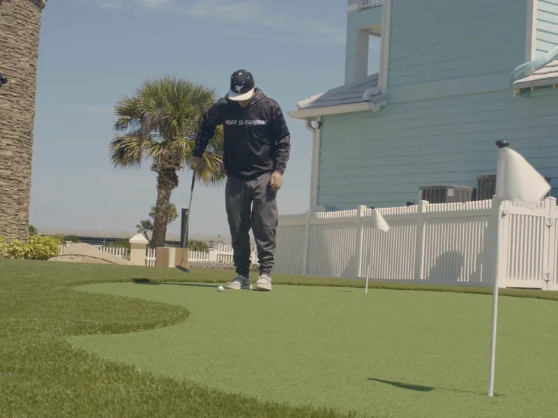 Vanilla Ice putting on a backyard green beside a pale blue house